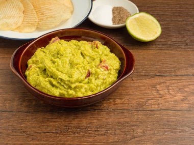 Tabaktaki taze guacamole sosu ve ahşap masadaki malzemelerin üst görüntüsü. Sağlıklı avokado yayılımı. Geleneksel Meksika hazırlığı kavramı