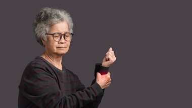 Gri arka planda dururken bilek ağrısı çeken yaşlı bir Asyalı kadın. Yaşlılar ve sağlık konsepti