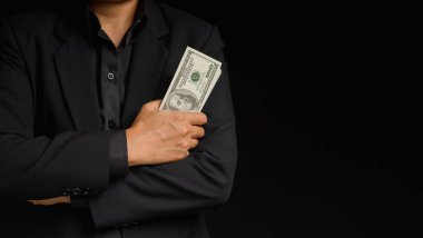 İş ve finans kavramı. Takım elbiseli bir işadamı, siyah bir geçmişle stüdyoda dururken elinde ABD banknotları tutuyordu. Kişisel krediler ve maaş kredileri. Metin için boşluk