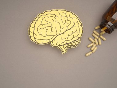 Kağıttan yapılmış beyin şekli ve gri arka planda şişesi olan ilaç kapsülleri. Alzheimer, Parkinson hastalığı, bunama, felç, nöbet ya da akıl sağlığı