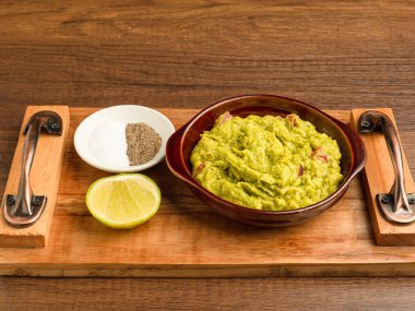 Tahta bir masanın üzerindeki tepside taze guacamole ile bir kase. Sağlıklı avokado yayılımı. Üst Manzara. Yakın plan fotoğraf. Geleneksel Meksika hazırlığı kavramı