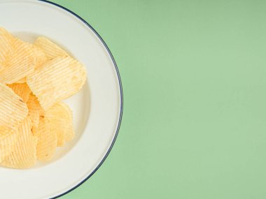 Yeşil arka planda beyaz bir tabakta patates cipsi ya da cips. Mesaj için yer var. Üst görünüm