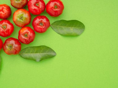 Açık yeşil zemin üzerinde olgun kırmızı acerola kirazları ve yeşil yaprakların üst görüntüsü. Yüksek C vitamini ve antioksidan meyveler. Mesaj için yer var. Yakın plan fotoğraf. Sağlıklı meyve kavramı