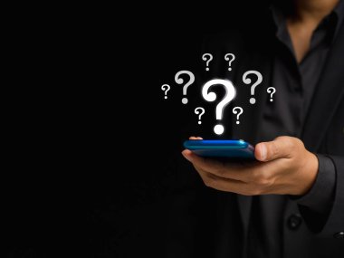 Soru işareti konsepti. Siyah arka planda dururken sanal ekranda soru işaretleri olan bir akıllı telefon kullanan bir işadamı
