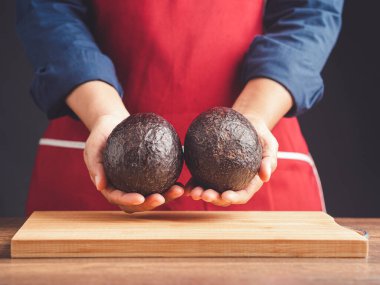 The chef hands holding a fresh two avocado while standing in the kitchen. Healthy fruit and food eating concept. Close-up photo clipart