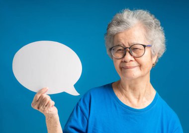 Yaşlı bir Asyalı kadının portresi boş bir konuşma balonu tutuyor ve mavi arka planda dururken kameraya gülümsüyor. Mesaj için yer var. Konuşma balonu konsepti