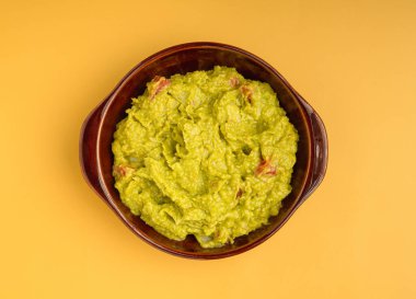 Sarı arka plan üzerinde bir kasede taze guacamole manzarası. Sağlıklı avokado yayılımı. Düz yatıyordu. Geleneksel Meksika hazırlığı kavramı