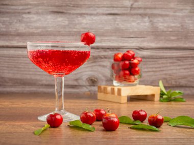 Taze kirazlı, buzlu, taze bir bardak. Tahta bir masada olgun kırmızı acerola kirazı ve yeşil yapraklar. Soğuk içecek ferahlatıcı. Yaz partisi. Yüksek C vitamini ve antioksidan meyvesi