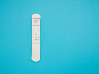 Mavi arka plan üzerinde SARS-COV-2 tükürük Antijen Hızlı Test Kiti (ATK) ile Covid-19 Pozitif test sonucu. Coronavirus bulaşıcı koruyucusu için kendini test ediyor. Üst görünüm