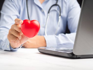 Kardiyoloji konsepti. Hastanede otururken kırmızı kalp şeklini koruyan el doktorunun yakın çekimi. Mesaj için yer var. Yakın plan fotoğraf. Sağlık ve tıbbi kavramsal