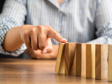 İş konseptinde risk ve strateji. Ofiste otururken tahta bir bloğu domino taşının üzerine iterek yakın plan. Yakın plan fotoğraf.