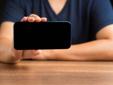 Masada otururken boş bir ekran akıllı telefonu tutan elin yakın çekimi. Mesaj için yer var. Teknoloji ve iletişim konsepti