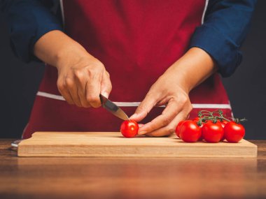 Şef mutfakta dururken kiraz domateslerini olgun kiraz domatesleriyle ahşap bir kesim tahtasının üzerinde dilimliyor. Sağlıklı meyve ve yiyecek yeme konsepti. Yakın plan fotoğraf.