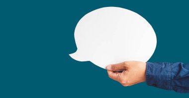 Stüdyonun mavi arka planına karşı beyaz bir konuşma balonu tutan yakın plan. Yakın plan fotoğraf. Metin için boşluk