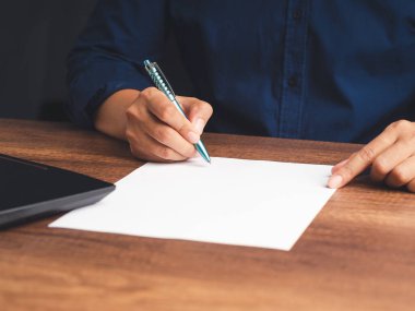 Ofiste otururken ahşap bir masanın üzerinde kağıt üzerine bir kalem tutarken yakın plan. Mesaj için yer var. İş ve strateji planlama kavramı