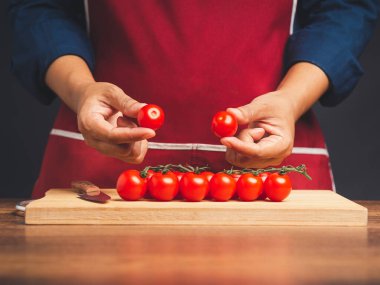 Aşçı elleri mutfakta dururken taze kiraz domatesleri ve bir yığın domatesi ahşap kesme tahtasının üzerinde tutuyor. Sağlıklı meyve ve yiyecek yeme konsepti. Yakın plan fotoğraf.