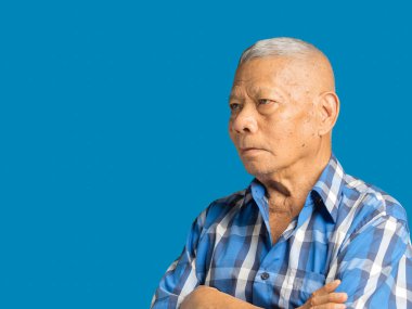 Mavi gömlekli yaşlı bir Asyalı adamın portresi stüdyoda mavi bir arka planda dikilirken çapraz ve uzağa bakıyor. Mesaj için yer var. Yaşlılar ve sağlık konsepti