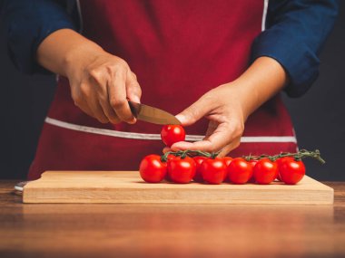 Şef mutfakta dururken kiraz domateslerini olgun kiraz domatesleriyle ahşap bir tahta üzerinde dilimliyor. Sağlıklı meyve ve yiyecek yeme konsepti. Yakın plan fotoğraf.