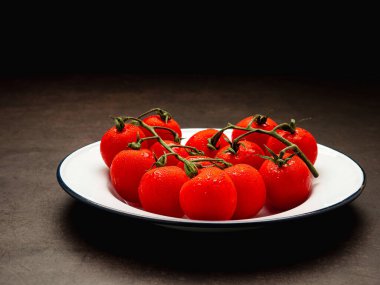 Kırmızı olgun taze vişneli domatesler ve yeşil saplı domatesler bağbozumu arka planında beyaz bir tabakta. Üst Manzara. Mesaj için yer var. Yakın plan fotoğraf.