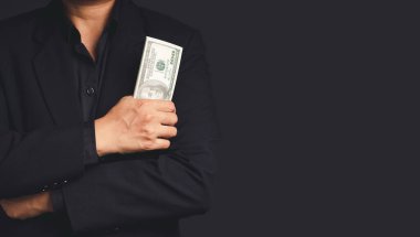 Siyah takım elbiseli bir işadamı, stüdyoda siyah bir arka planda dururken Amerikan doları banknotlarını tutuyor. Mesaj için yer var. İş, finans ve kişisel kredi kavramları