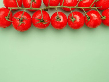 Yeşil zemin üzerinde yeşil saplı taze kırmızı kiraz domatesleri. Üst Manzara. Yakın plan fotoğraf. Sağlıklı gıda ve meyve kavramı