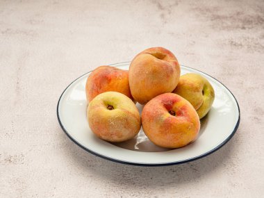 Beton zeminin üzerinde beyaz bir tabakta taze olgun şeftali meyveleri. Üst Manzara. Yakın plan fotoğraf. Sağlıklı gıda ve meyve kavramı