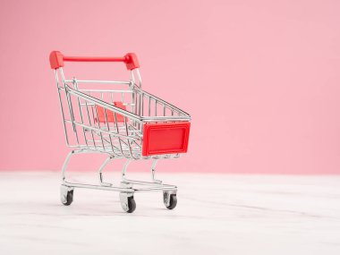 Pembe arka planlı mermer zeminde mini bir alışveriş arabası. İş ve e-ticaret kavramı