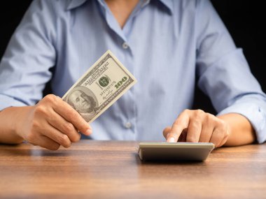 Para ve finans kavramı. Amerikan doları banknotlarını elinde tutan ve ofiste otururken hesap makinesi kullanan bir iş adamı.