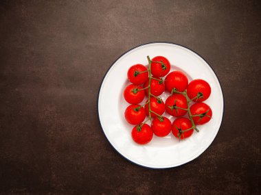 Bir grup olgun kırmızı kiraz domatesleri ve yeşil saplı domatesler bağbozumu arka planında beyaz bir tabakta. Üst Manzara. Mesaj için yer var. Yakın plan fotoğraf.