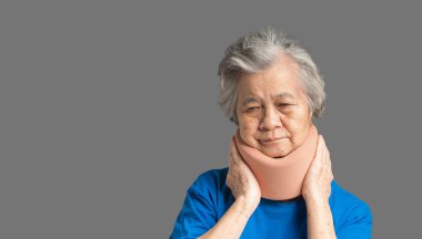 Gri arka planda dururken boyun ağrısı çektiği ve boyun eğdiği için yumuşak boyunluk takan son sınıf bir kadının portresi. Tıbbi ve sağlık hizmeti kavramı