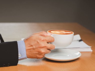Ofiste çalışan bir iş adamı elinde bir fincan kahveyle oturuyor. Yakın plan fotoğraf. İçecek ve rahatlama kavramı
