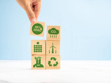 2050 'de net sıfır karbondioksit emisyonu hedefi. Açık yeşil zemin üzerinde yeşil simgelerle ahşap bir küpün el ele tutuşması. İklim-nötr uzun vadeli strateji. Metin için boşluk