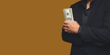İş ve finans kavramı. Takım elbiseli bir işadamı stüdyoda dururken ABD banknotlarını turuncu arka planda tutuyor. Kişisel krediler ve maaş kredileri. Metin için boşluk