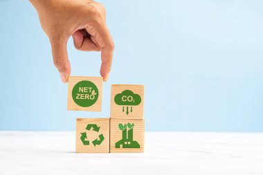 2050 'de net sıfır karbondioksit emisyonu hedefi. Açık yeşil zemin üzerinde yeşil simgelerle ahşap bir küpün el ele tutuşması. İklim-nötr uzun vadeli strateji. Metin için boşluk