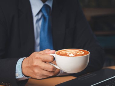 Ofiste çalışan bir iş adamı elinde bir fincan kahveyle oturuyor. Yakın plan fotoğraf. İçecek ve rahatlama kavramı