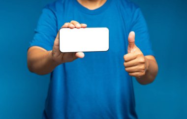 Boş beyaz ekranlı, yatay bir cep telefonu tutan ve mavi arka planda dururken başparmaklarını gösteren bir el. Müşteri geribildirimi, hizmet değerlendirmesi, deneyim ve tatmin kavramı