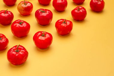 Sarı arka planda izole edilmiş olgun kırmızı acerola kirazlarının üst görüntüsü. Yüksek C vitamini ve antioksidan meyveler. Mesaj için yer var. Yakın plan fotoğraf. Sağlıklı meyve kavramı