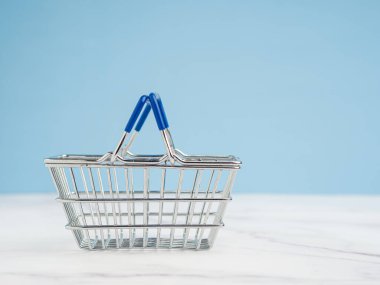 Açık mavi zemin üzerinde boş bir mini alışveriş arabası. Yan görüş. Mesaj için yer var. İş ve e-ticaret kavramı