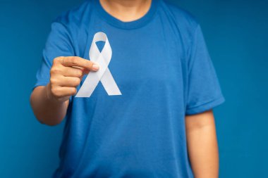 Bir kadın el mavi arka planda beyaz bir kurdele tutuyor. Akciğer kanseriyle mücadelenin sembolü. Kasım, akciğer kanseri farkındalığı ayı