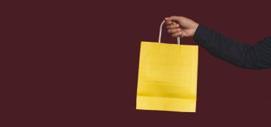 Kırmızı arka planda sapı olan sarı bir kese kağıdını tutarken. Paketleme şablonu modeli. Teslimat hizmeti, alışveriş ve reklam alanı kavramı