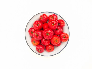Beyaz arka planda beyaz bir tabakta olgun kırmızı acerola kirazlarının üst görüntüsü. Yüksek C vitamini ve antioksidan meyveler. Mesaj için yer var. Yakın plan fotoğraf. Sağlıklı meyve kavramı