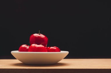 Ahşap bir masada, siyah arka planda duran kirazların içinde olgunlaşmış kırmızı acerola. Yüksek C vitamini ve antioksidan meyveler. Mesaj için yer var. Yakın plan. Sağlıklı meyve kavramı