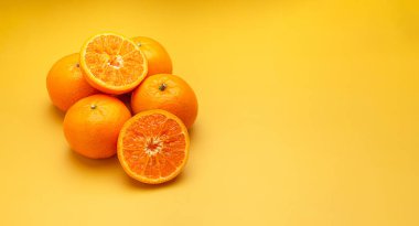 Sarı bir zemin üzerinde taze portakal ve yarım meyve yığını ve metin için kopya alanı. Sağlıklı meyve kavramı. Yakın plan fotoğraf.