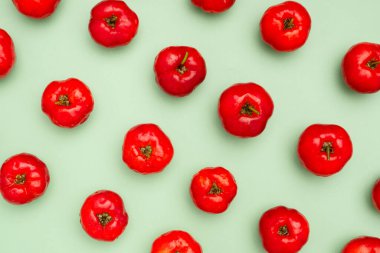 Açık yeşil zemin üzerinde izole edilmiş olgun kırmızı acerola kirazlarının üst görüntüsü. Yüksek C vitamini ve antioksidan meyveler. Mesaj için yer var. Yakın plan fotoğraf. Sağlıklı meyve kavramı