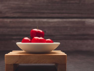 Olgun kırmızı acerola kirazları ahşap bir masada bir tabakta. Yüksek C vitamini ve antioksidan meyveler. Mesaj için yer var. Yakın plan. Sağlıklı meyve kavramı