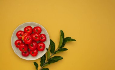 Olgun kırmızı acerola kirazları ve turuncu arka planda yeşil yapraklar. Yüksek C vitamini ve antioksidan meyveler. Mesaj için yer var. Yakın plan fotoğraf. Sağlıklı meyve kavramı