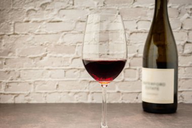 Kırmızı şarap kadehi ve beyaz tuğla kaplama arka planlı şişe. Mesaj için yer var. Yakın plan fotoğraf. İçecek ve rahatlama kavramı