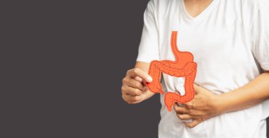 Kolon sembolü tutan ve mide ağrısına dokunan bir elin yakın çekimi. Gastrointestinal sistem hastalığı. Karın ağrısı mide ülserine ve daha fazlasına neden olur. Metin için boşluk