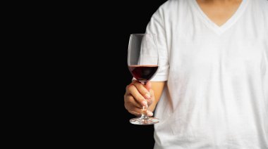 Gri arka planda dururken kırmızı şarap kadehini tutarken yakın plan. Mesaj için yer var. İçecek ve rahatlama kavramı