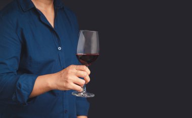 Gri arka planda dururken kırmızı şarap kadehini tutarken yakın plan. Mesaj için yer var. İçecek ve rahatlama kavramı